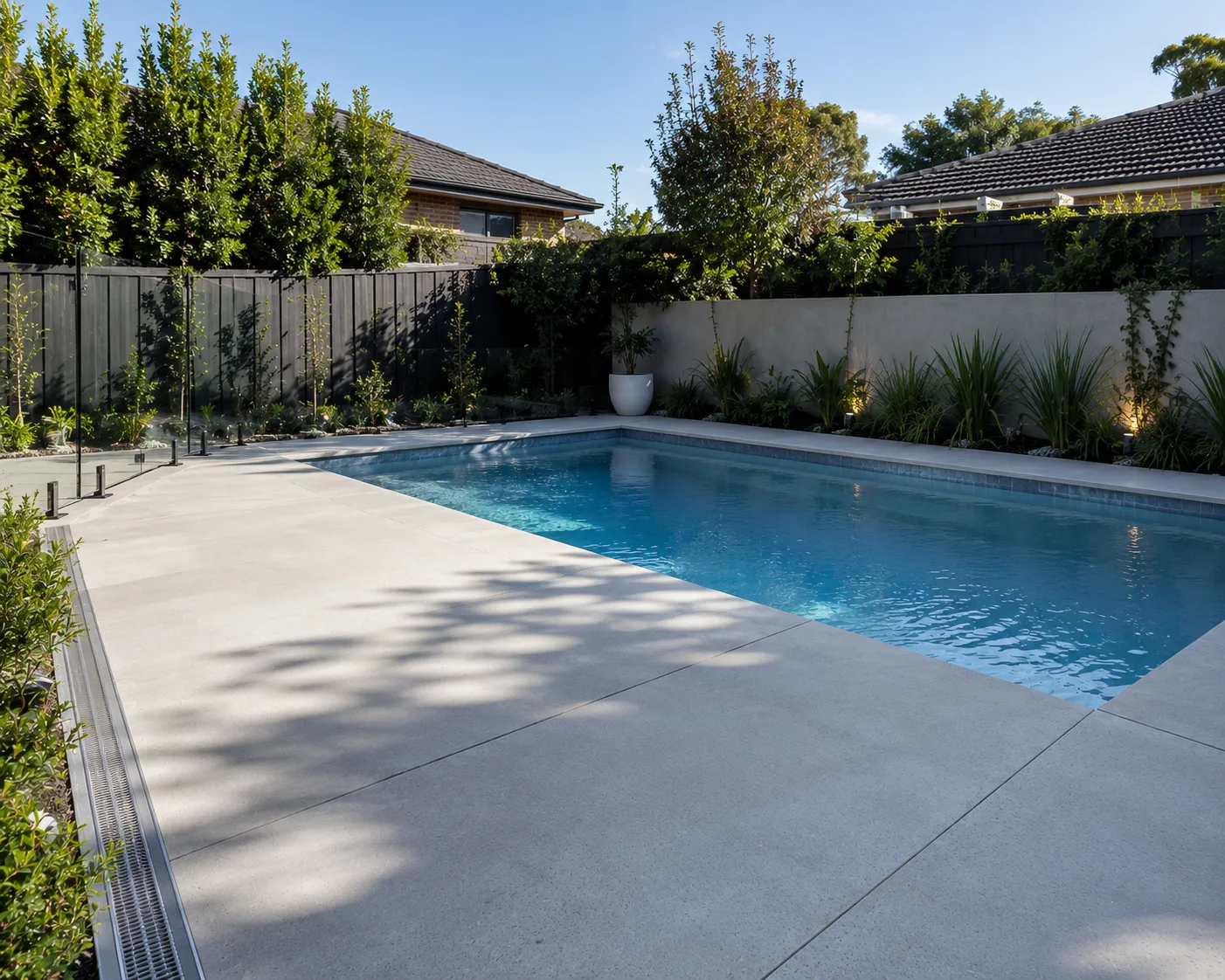 Concrete pool surround and paving along a fenced backyard pool