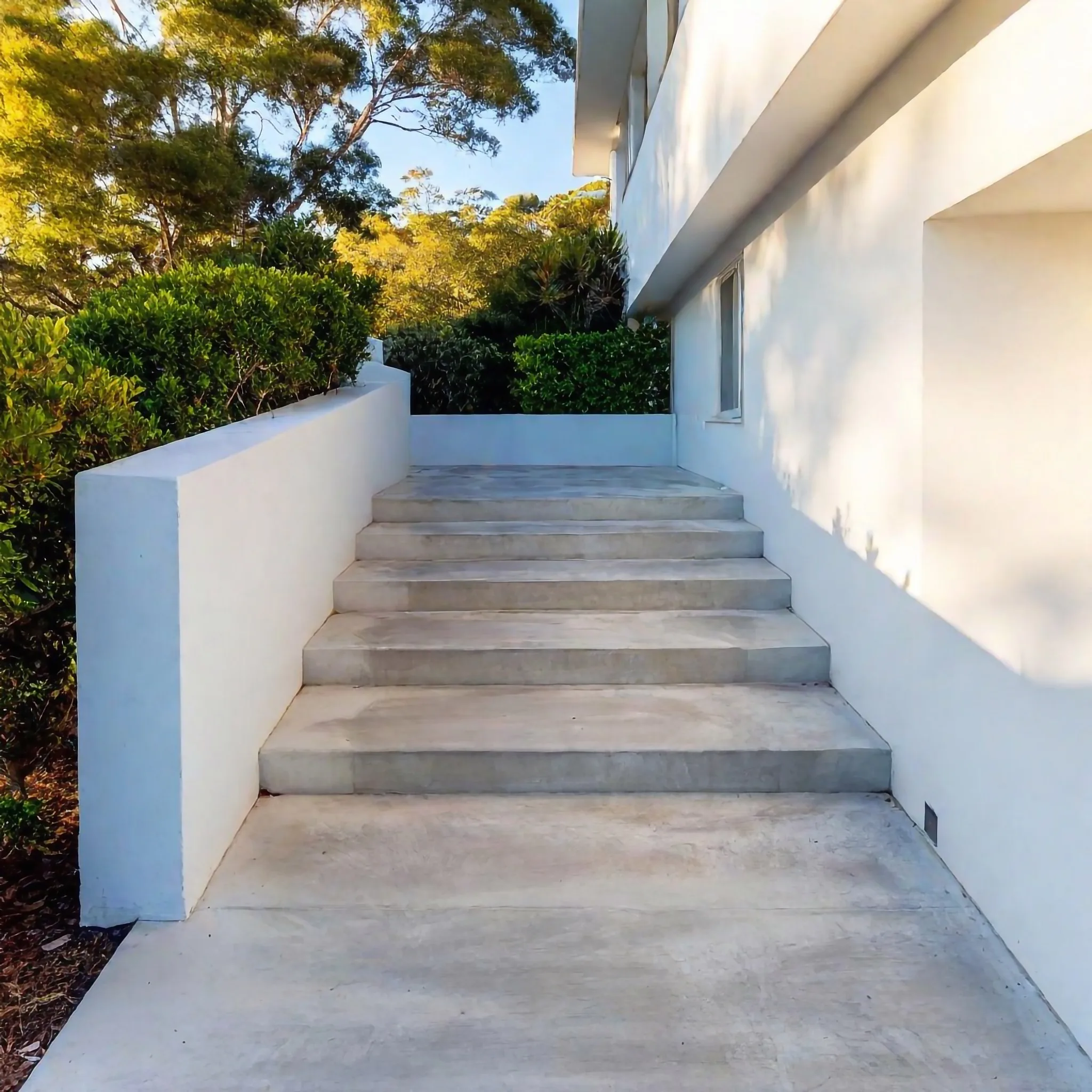 Wide concrete stairs leading up beside a white rendered home
